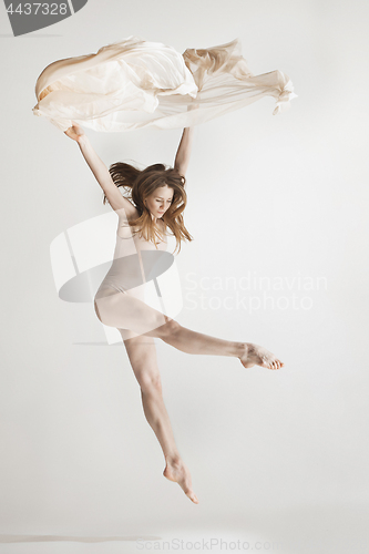 Image of Young beautiful dancer in beige swimsuit dancing on gray background