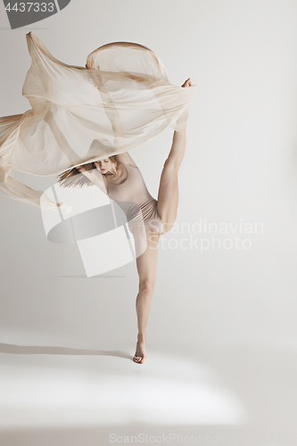 Image of Young beautiful dancer in beige swimsuit dancing on gray background