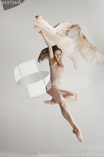 Image of Young beautiful dancer in beige swimsuit dancing on gray background