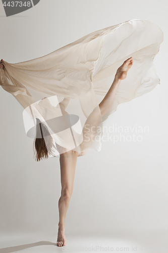 Image of Young beautiful dancer in beige swimsuit dancing on gray background