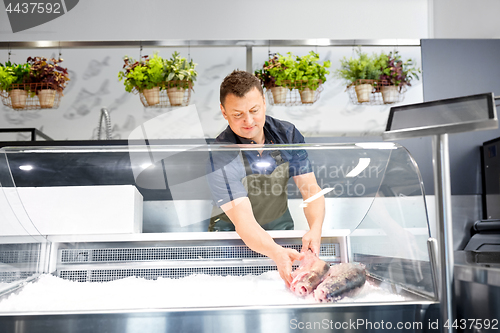 Image of male seller putting trout to fridge at fish shop