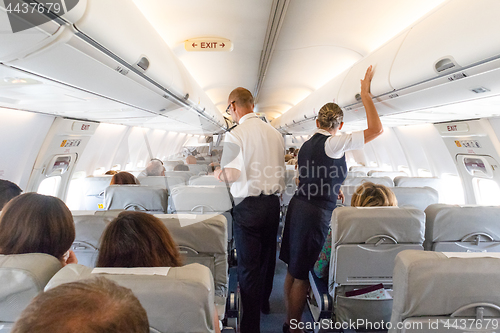 Image of Interior of large commercial airplane with stewardesses serving passengers on seats during flight.