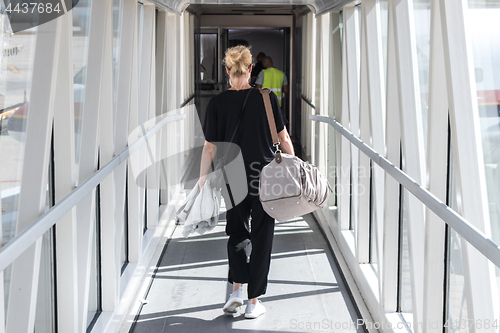 Image of Female passenger carrying the hand luggage bag, walking the airplane boarding corridor.