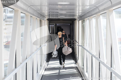 Image of Female passenger carrying the hand luggage bag, walking the airplane boarding corridor.