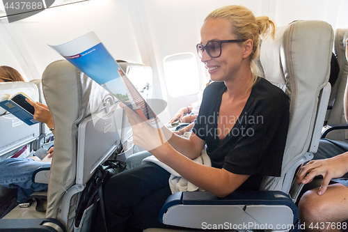 Image of Woman reading magazine on airplane during flight.