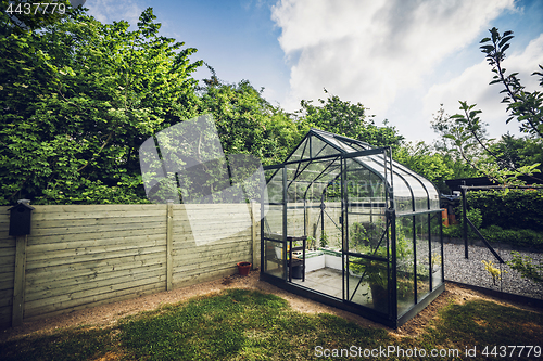 Image of Greenhouse in a garden with trees behind