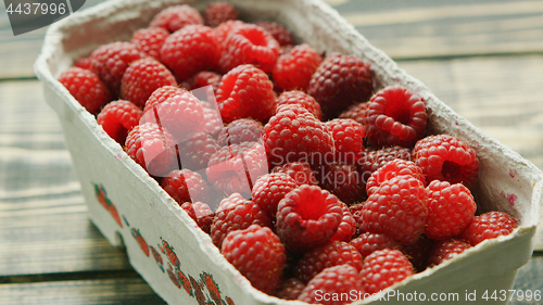 Image of Container with ripe raspberry on wooden desk 