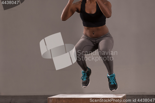 Image of black woman is performing box jumps at gym
