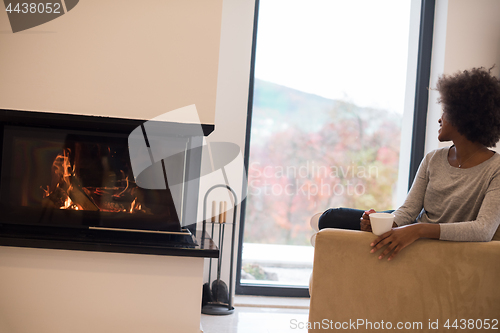 Image of black woman drinking coffee in front of fireplace