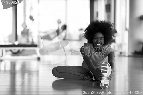 Image of woman in a gym stretching and warming up man in background worki