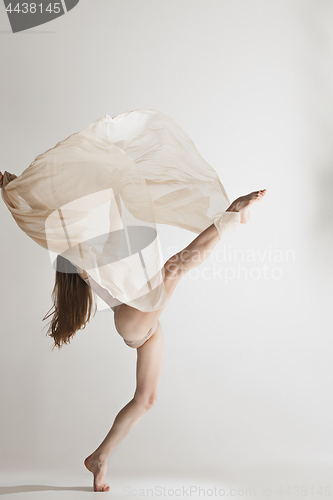 Image of Young beautiful dancer in beige swimsuit dancing on gray background