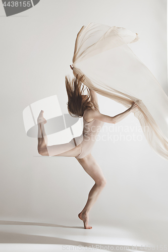 Image of Young beautiful dancer in beige swimsuit dancing on gray background