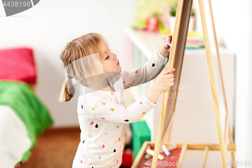 Image of happy little girl drawing on chalk board at home