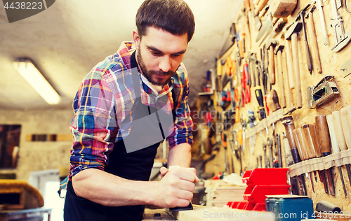 Image of carpenter working with plane and wood at workshop