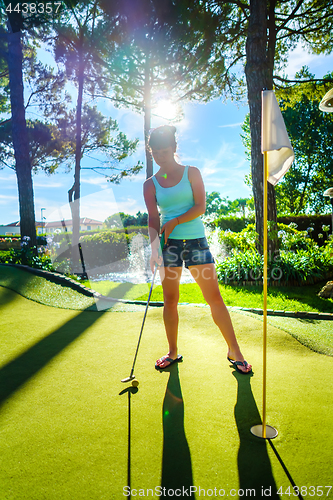 Image of Mini Golf - Woman playing Golf on green grass at sunset