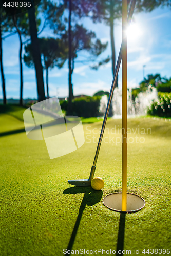 Image of Mini Golf yellow ball with a bat near the hole at sunset