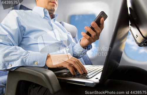 Image of businessman with smartphone and laptop in plane