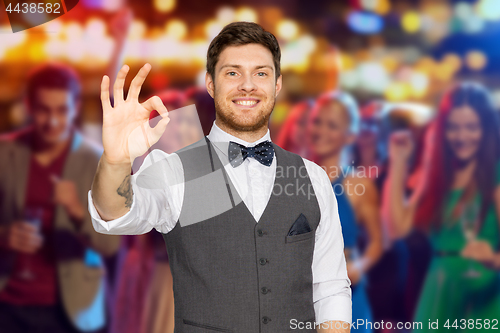 Image of man in suit showing ok sign over night club party