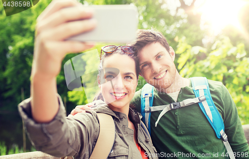 Image of couple with backpacks taking selfie by smartphone