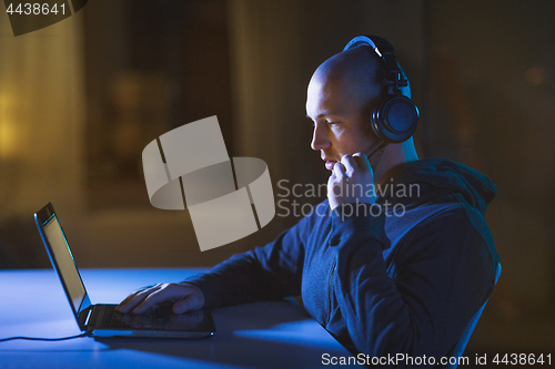 Image of hacker in headset typing on laptop in dark room