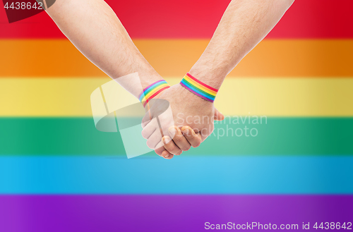 Image of hands of couple with gay pride rainbow wristbands