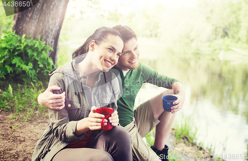 Image of happy couple with cups drinking in nature