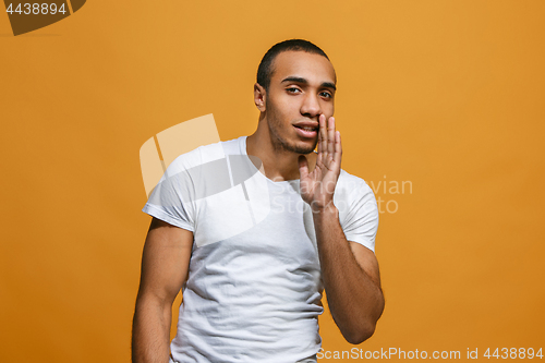 Image of The young man whispering a secret behind her hand over orange background