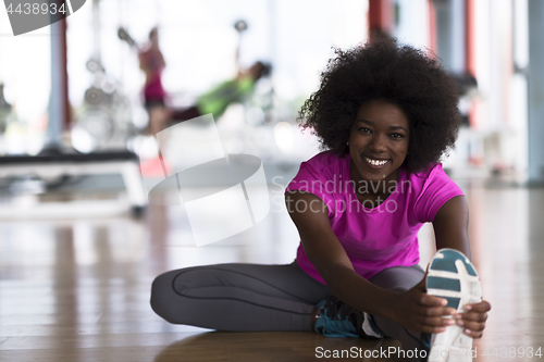 Image of woman in a gym stretching and warming up man in background worki
