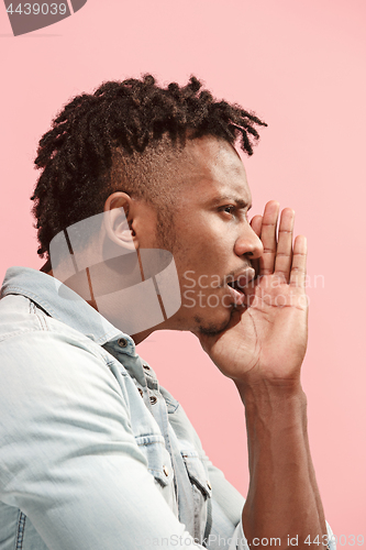 Image of The young Afro-American man whispering a secret behind her hand over pink background