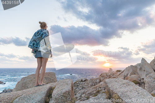 Image of Solo young female traveler watches a beautiful sunset on spectacular rocks of Capo Testa, Sardinia, Italy, a popular summer traveling destination in Europe.