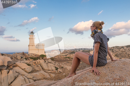 Image of Solitary young female traveler watches a beautiful sunset over lighthouse and spectacular rock formations of Capo Testa, Sardinia, Italy.