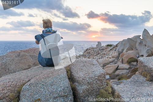 Image of Solo young female traveler watches a beautiful sunset on spectacular rocks of Capo Testa, Sardinia, Italy, a popular summer traveling destination in Europe.