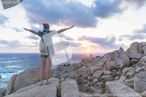 Image of Female traveler, arms rised to the sky, watches a beautiful sunset on spectacular rocks of Capo Testa, Sardinia, Italy.