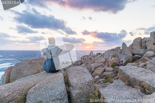 Image of Solo young female traveler watches a beautiful sunset on spectacular rocks of Capo Testa, Sardinia, Italy, a popular summer traveling destination in Europe.