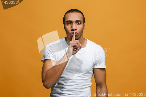 Image of The young man whispering a secret behind her hand over orange background