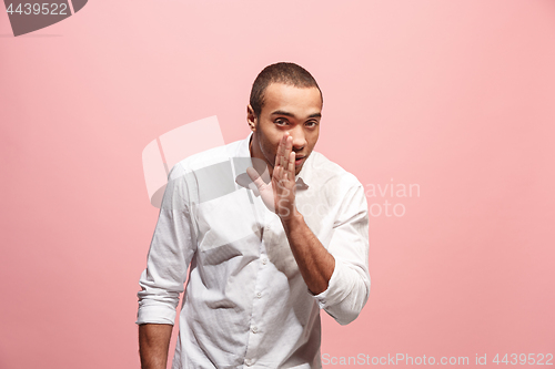 Image of The young man whispering a secret behind her hand over pink background