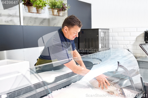Image of male seller putting trout to fridge at fish shop