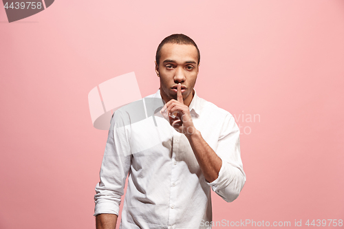 Image of The young man whispering a secret behind her hand over pink background