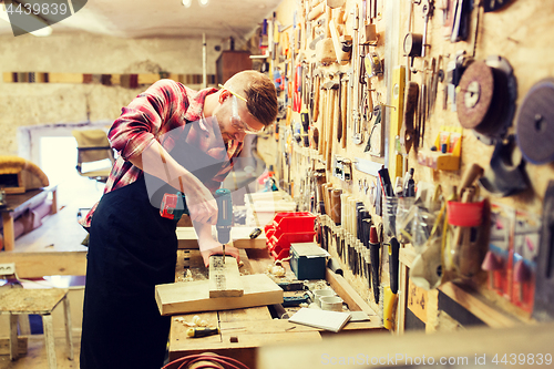 Image of carpenter with drill drilling plank at workshop