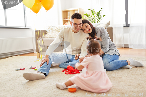 Image of baby girl with birthday gift and parents at home