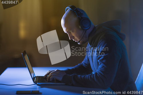 Image of hacker in headset typing on laptop in dark room