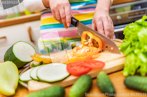 Image of Female hands of housewife with a knife cut fresh bell pepper on 