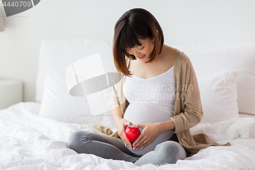 Image of happy pregnant asian woman with red heart in bed