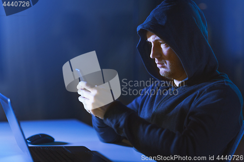 Image of hacker with laptop and smartphone in dark room