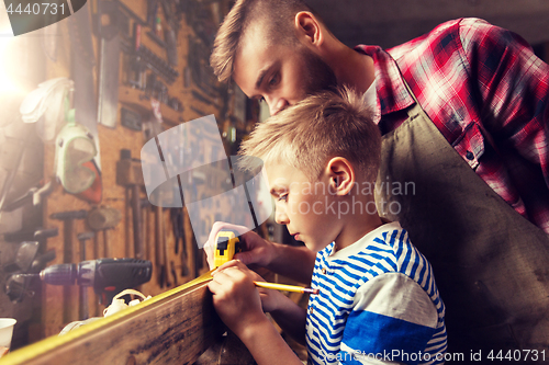 Image of father and son with ruler measure wood at workshop