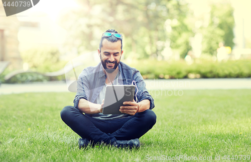 Image of man with earphones and tablet pc sitting on grass