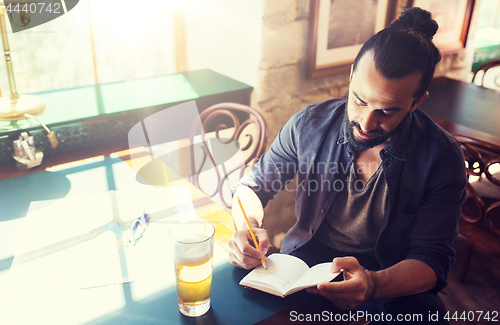 Image of man with beer writing to notebook at bar or pub