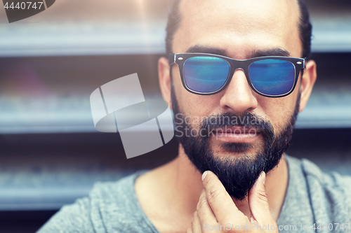 Image of man in sunglasses touching beard on city street