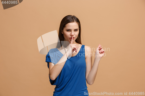 Image of The young woman whispering a secret behind her hand over paslel background