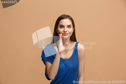 Image of The young woman whispering a secret behind her hand over pastel background